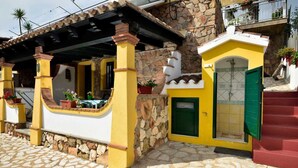 A yellow and white building with a stone facade, a small porch with potted plants, and a green door.