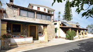 A two-story building with a stone facade, a balcony, and a covered entrance area with potted plants.