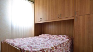 A single bed with a floral bedspread in a room with wooden cabinets and a curtain.