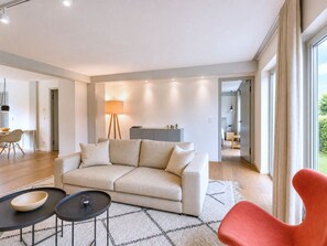 A modern living room with a sofa, two coffee tables, a lamp, and a view of the outdoors.