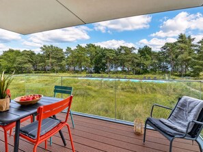 Un balcón con mesa, sillas y vistas a una piscina y árboles.