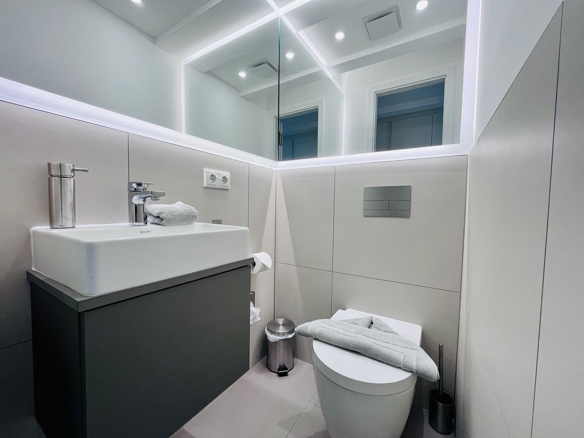 Un baño moderno con lavamanos, espejo y retrete blancos.