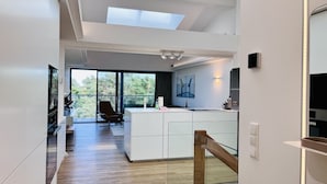 A modern kitchen with a central island, large windows, and a staircase leading to an upper level. - "Purbaltic" maisonette apartment with lake view and sauna, completed in 2022 (Prora)