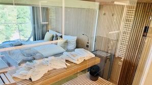 A modern bedroom with a bed, a wooden bench, and a glass partition. - "Purbaltic" maisonette apartment with lake view and sauna, completed in 2022 (Prora)