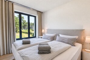 Habitación de hotel con dos camas, un ventanal grande y vistas a la vegetación.
