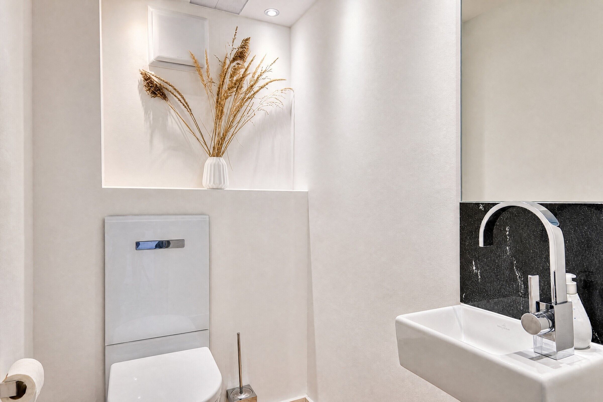 Un baño moderno con un lavamanos blanco, un espejo y un inodoro.