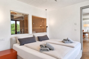 A modern bedroom with two beds, a wooden headboard, a window, and a view of the outdoors.