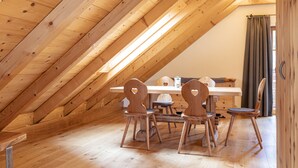 A wooden dining area with a table and chairs, a window with curtains, and a sloped ceiling with wooden beams. - AlpiNest Hochgolling 2 Loft Apartment (Mariapfarr)