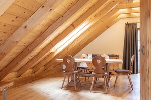 Un comedor de madera con una mesa y sillas, una ventana con cortinas, y un techo inclinado con vigas de madera.