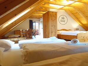 A cozy attic bedroom with wooden beams, a dining area, and a bed with neatly made linens.