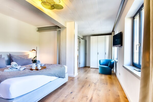A modern hotel room with a large bed, a blue armchair, and a TV mounted on the wall. - Luxury vacation apartment Meerlounge 15 in Prora Düne 7 with sea view balconies (Prora)