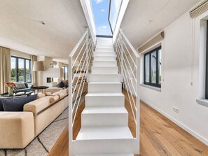 Et moderne interiør med en hvid trappe i midten, en sofaarrangement og et spiseområde.