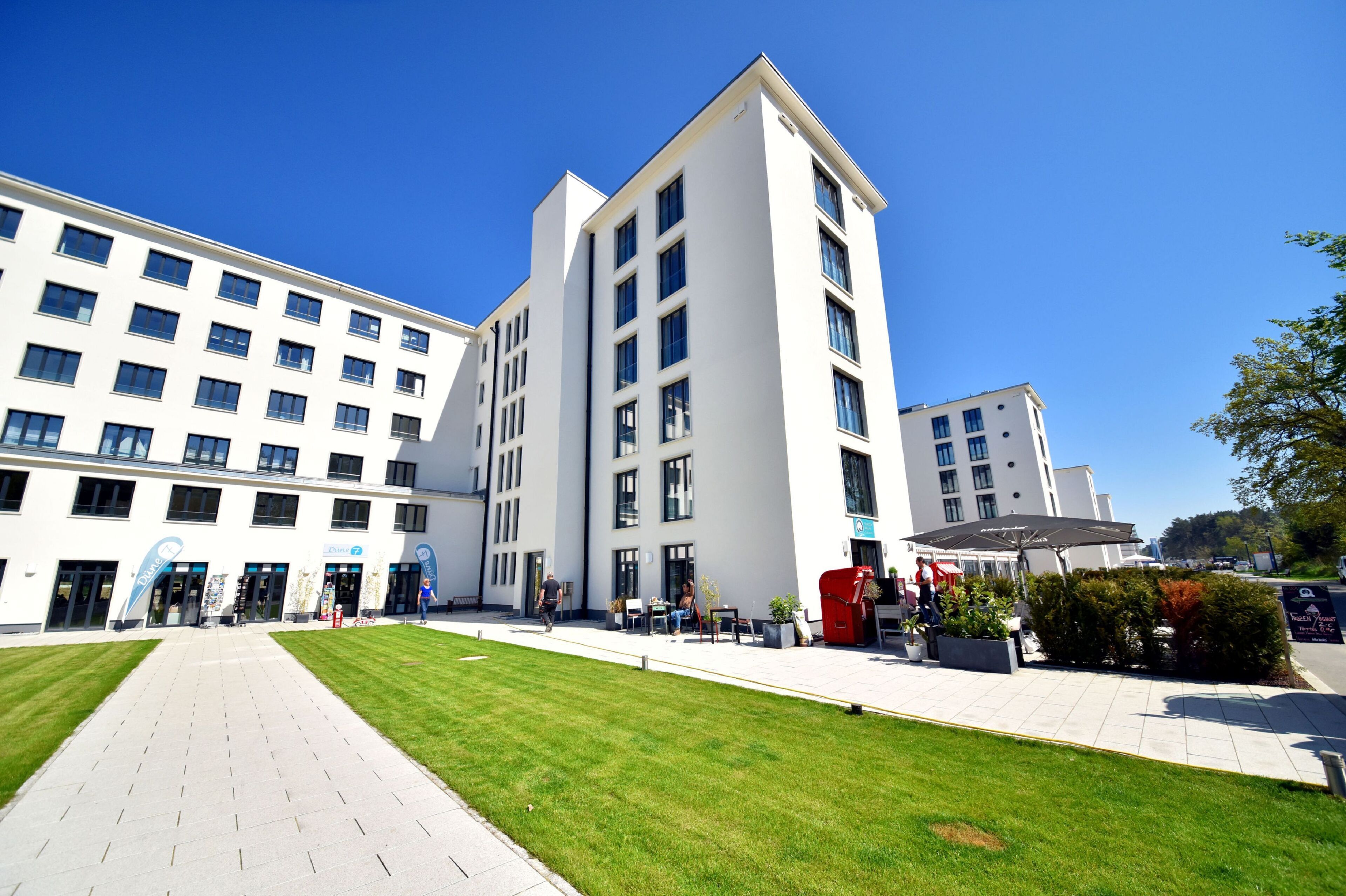 A modern building with multiple floors, a central courtyard with seating, and a clear blue sky.