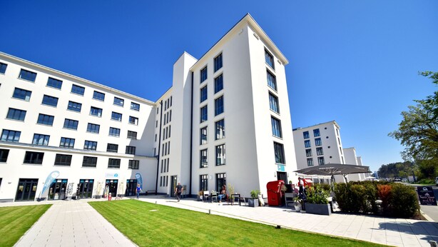 A modern building with multiple floors, a central courtyard with seating, and a clear blue sky.