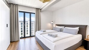 Habitación de hotel moderna con una cama grande, una mesita de noche, una lámpara y vistas a la ciudad.