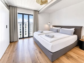 Et moderne hotelværelse med en stor seng, et sengebord, en lampe og udsigt over byen.