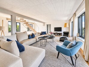 A modern living room with a sofa, armchair, coffee table, TV, and a staircase.