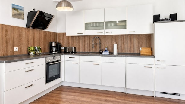 Eine moderne Küche mit weißen Schränken, einem eingebauten Backofen und einer Kaffeemaschine.
