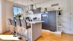 A modern kitchen with a central island, bar stools, pendant lights, and a built-in oven.