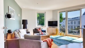 A modern living room with a sofa set, a television, and a balcony with a view of the city.