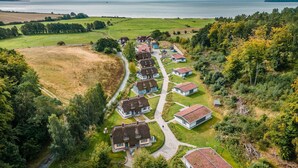 A coastal village with houses arranged in a row along a narrow road, surrounded by greenery and a view of the sea.