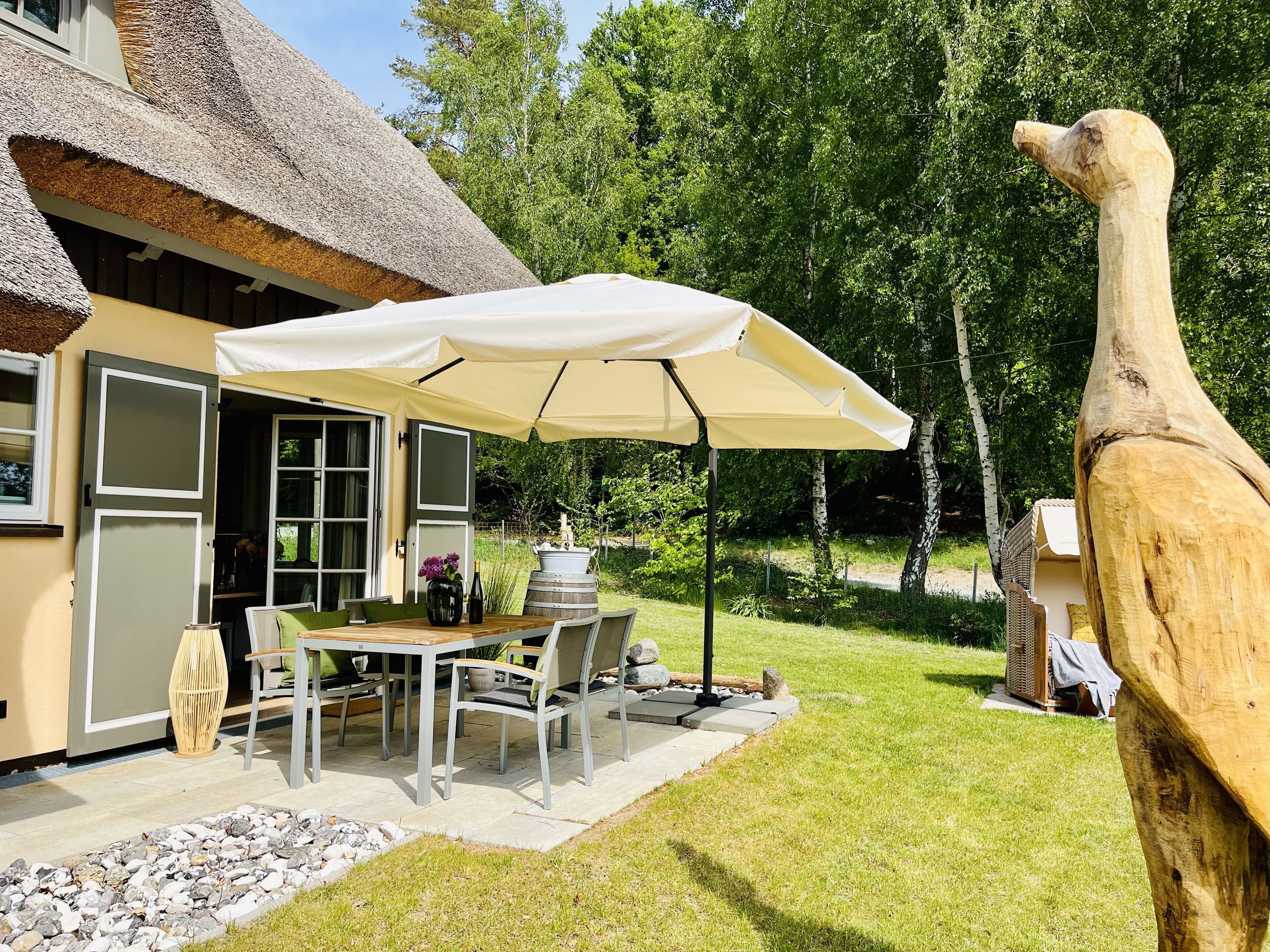A thatched-roof house with a patio table and chairs under a large umbrella.