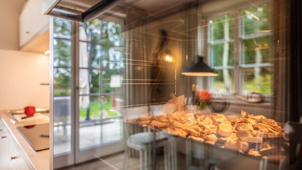 A modern kitchen with a glass partition, stainless steel appliances, and a view of the outdoors.