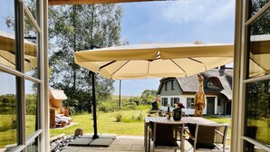 An outdoor patio area with a table and chairs under a large umbrella, a stone pathway, and a view of a house in the background.