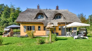 Una casa con techo de paja, un pequeño jardín con césped y mobiliario exterior.