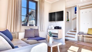 Una sala moderna con sofá, televisión y una escalera que lleva a otra habitación.