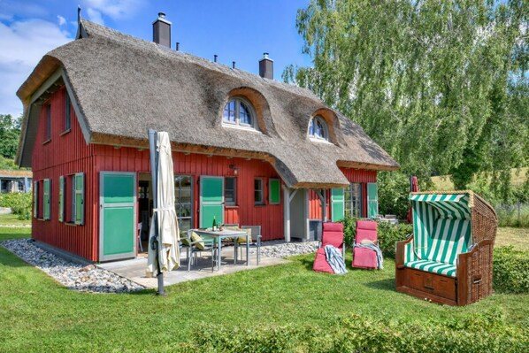 A red house with a thatched roof, green shutters, and a small patio with outdoor furniture. - New, modern, exclusive—that's how the Klein Stresow vacation village describes itself (Klein Stresow)