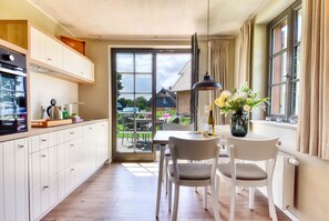 A modern kitchen with white cabinets, a dining area with two chairs, a table, and a view of the outside. - Newly built, modern, exclusive - that describes the Klein Stresow vacation village (Klein Stresow)
