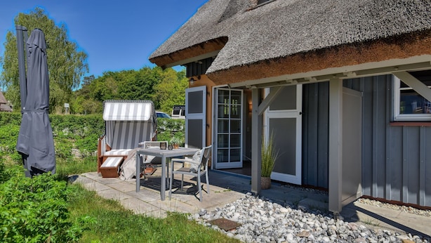 A house with a thatched roof, a patio with a table and chairs, and a covered outdoor area.