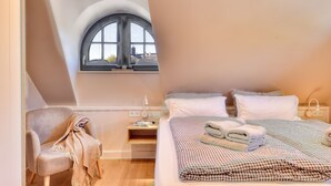 A bedroom with a bed, a chair, a nightstand, and a window with a view of the city.