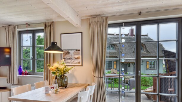 A dining area with a wooden table, white chairs, a hanging pendant light, and a vase with flowers. - Newly built, modern, exclusive - that describes the Klein Stresow vacation village (Klein Stresow)