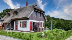 A traditional house with a thatched roof, a red and white facade, and a garden with a bird statue. - Newly built, modern, exclusive - that describes the Klein Stresow vacation village (Klein Stresow)