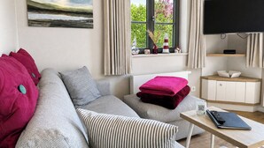A modern living room with a grey sofa, a flat-screen TV, a window with curtains, and a painting on the wall. - Newly built, modern, exclusive - that describes the Klein Stresow vacation village (Klein Stresow)