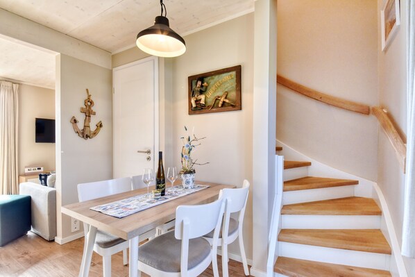 A dining area with a wooden table, white chairs, a chandelier, and a staircase. - Newly built, modern, exclusive - that describes the Klein Stresow vacation village (Klein Stresow)
