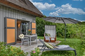 A thatched-roof building with a patio area featuring a table, chairs, and a lounge chair. - Newly built, modern, exclusive - that describes the Klein Stresow vacation village (Klein Stresow)
