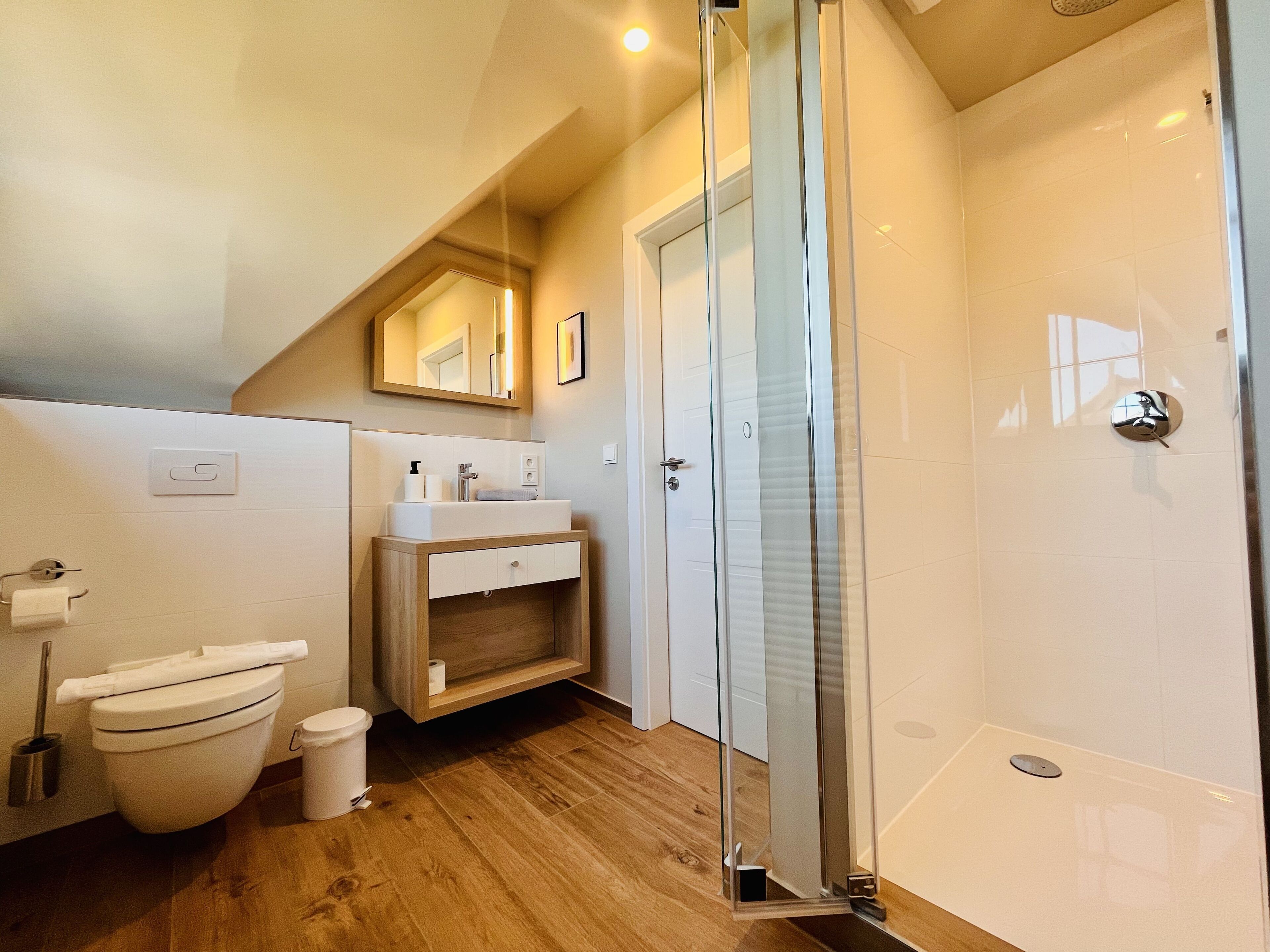Un baño moderno con tocador de madera, cabina de ducha de vidrio y inodoro blanco.