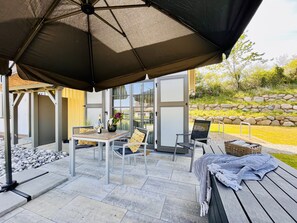 An outdoor patio with a table and chairs, a large umbrella, and a stone wall in the background. - Newly built, modern, exclusive - that describes the Klein Stresow vacation village (Klein Stresow)