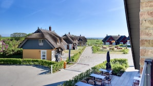 A courtyard with thatched-roof cottages, outdoor seating, and a clear view of the surrounding landscape. - Newly built, modern, exclusive - that describes the Klein Stresow vacation village (Klein Stresow)
