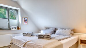 A bedroom with a large bed, a window with blinds, a bedside table, and a framed picture on the wall. - Newly built, modern, exclusive - that describes the Klein Stresow vacation village (Klein Stresow)