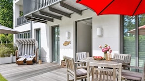Un patio moderno al aire libre con cubierta de madera, una mesa de comedor con sillas y una sillona a rayas.