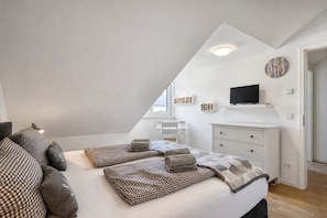 A bedroom with a sloped ceiling, a bed with checkered bedding, a television on a shelf, and a clock on the wall. - Home port: Your Baltic Sea retreat at Villa Sofie Binz - with roof terrace (Binz)