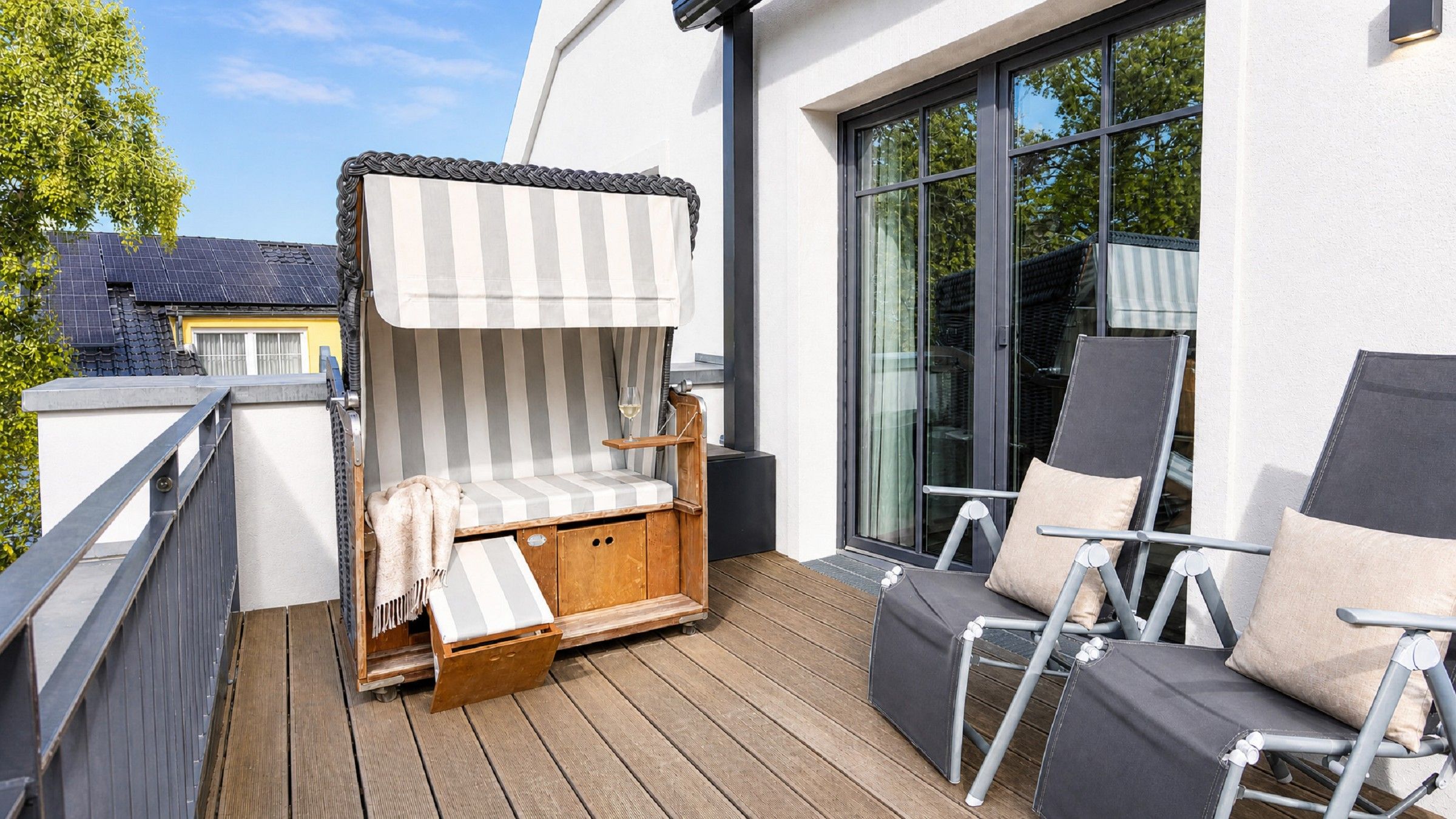 Eine Terrasse mit einem gestreiften Baldachin, einer Holzbank und zwei Liegestühlen.