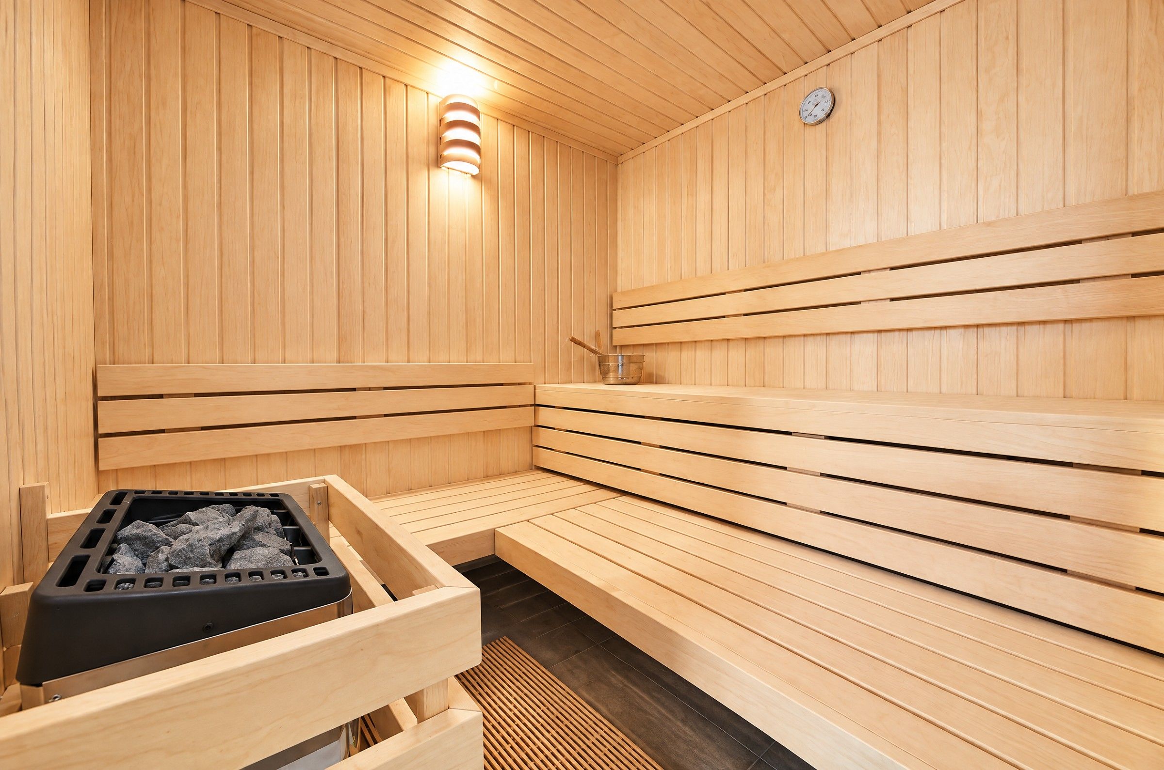 A sauna with wooden benches, a heating element, and a clock on the wall.
