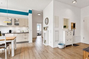A modern kitchen with white cabinets, a wooden dining table, and a hanging pendant light.