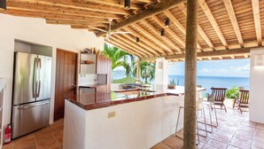 Una cucina con un'isola grande, frigorifero in acciaio inox, pensili in legno e vista sull'oceano.