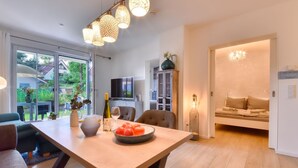 Un salon moderne avec une table à manger en bois, un canapé et un téléviseur. Une porte vitrée donne accès à un jardin.
